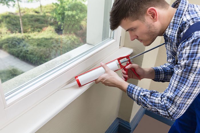 Man sealing bathroom window with silicone sealant- how to warm up your bathroom for winter