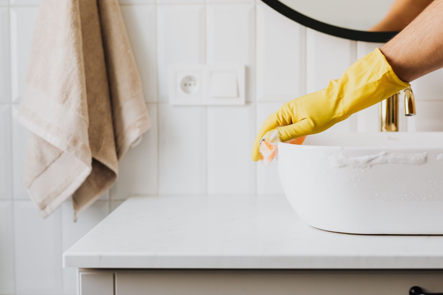 rubber gloved hand cleaning bathroom sink with sponge