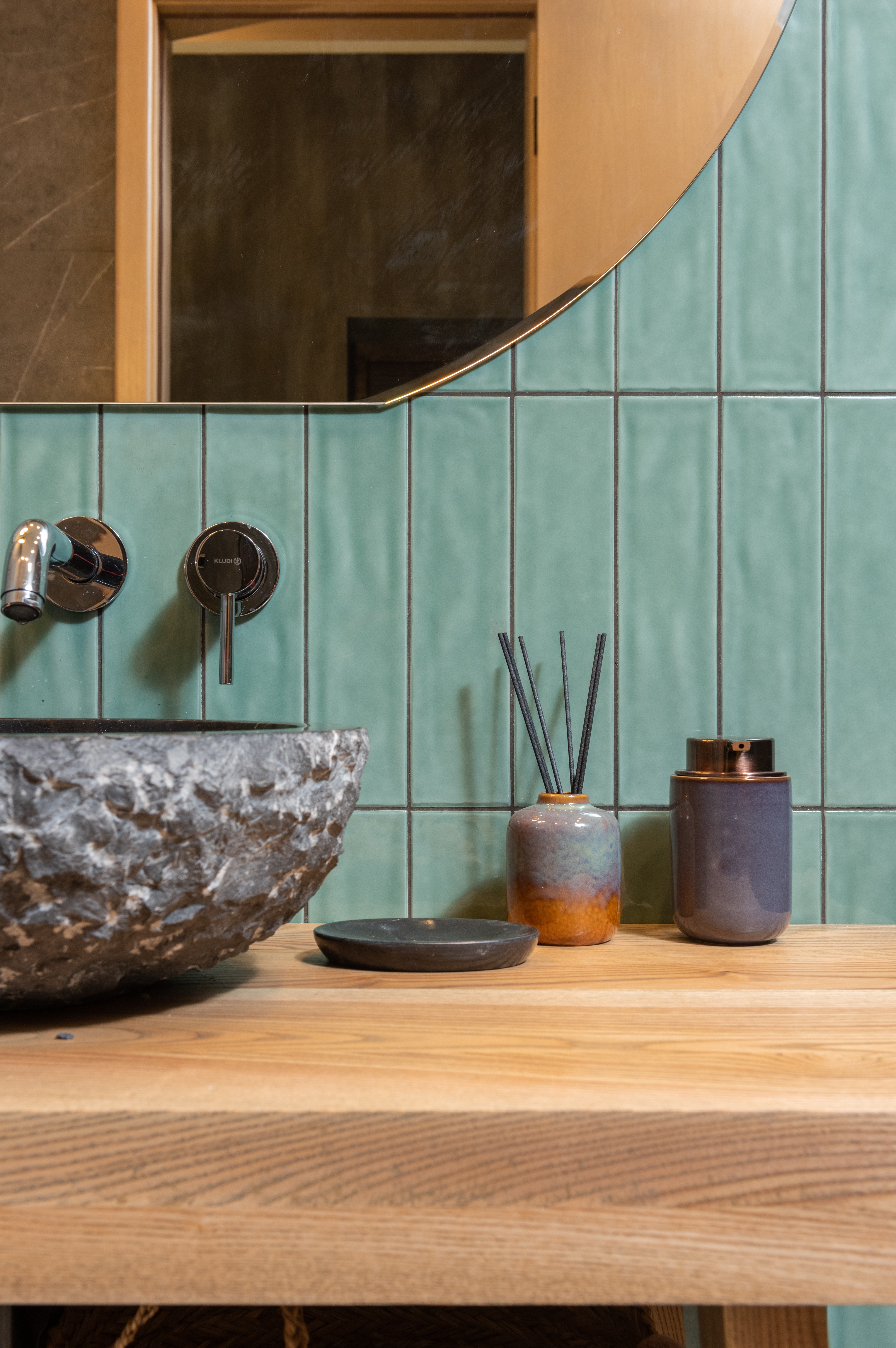 Glossy pastel green vertical tiles positioned on the wall behind a vanity unit with a countertop basin and a mirror.