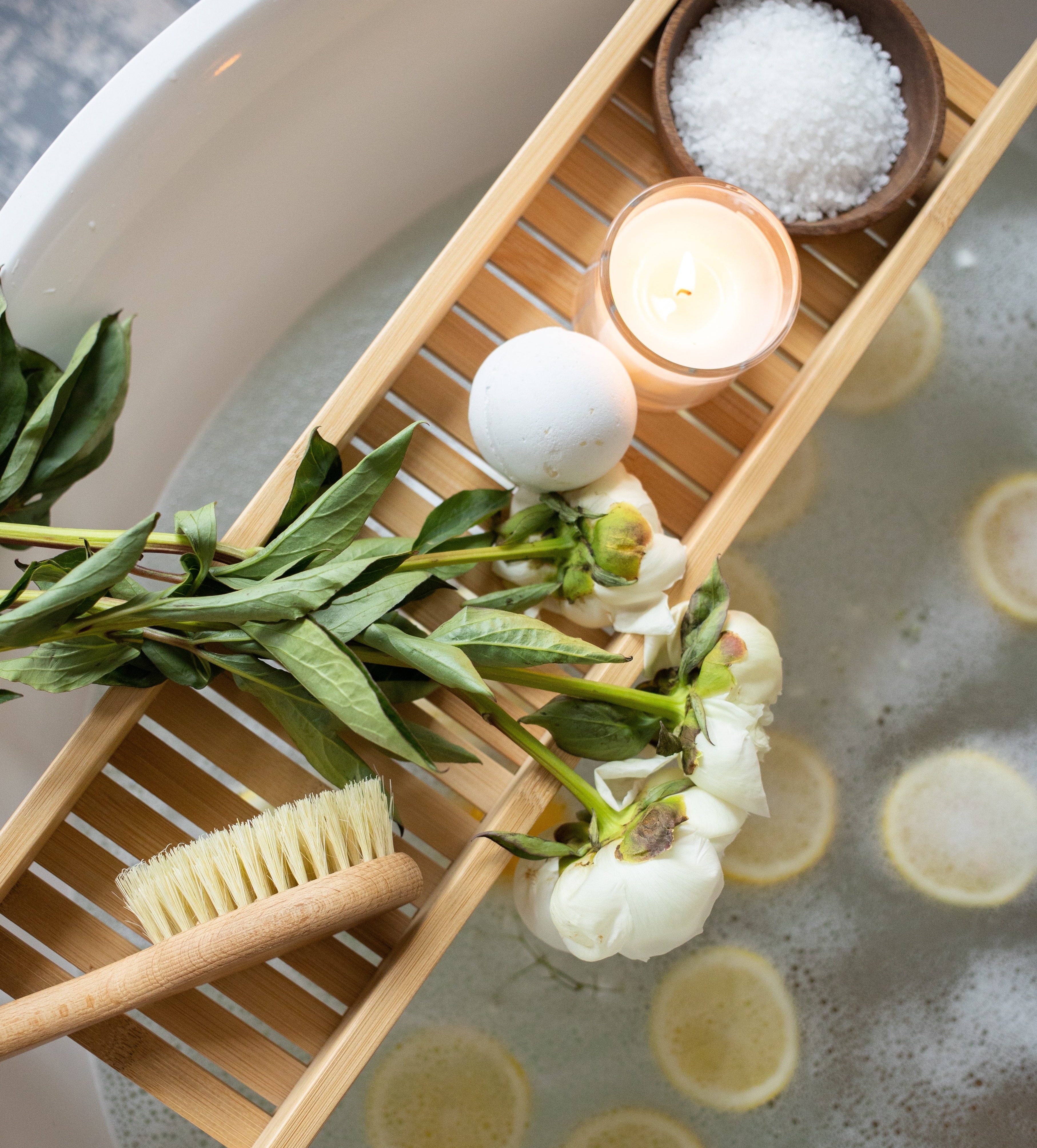 Tray with candles, bath bomb, bath salts and flowers on bathtub Tray with candles, bath bomb, bath salts and flowers on bathtub