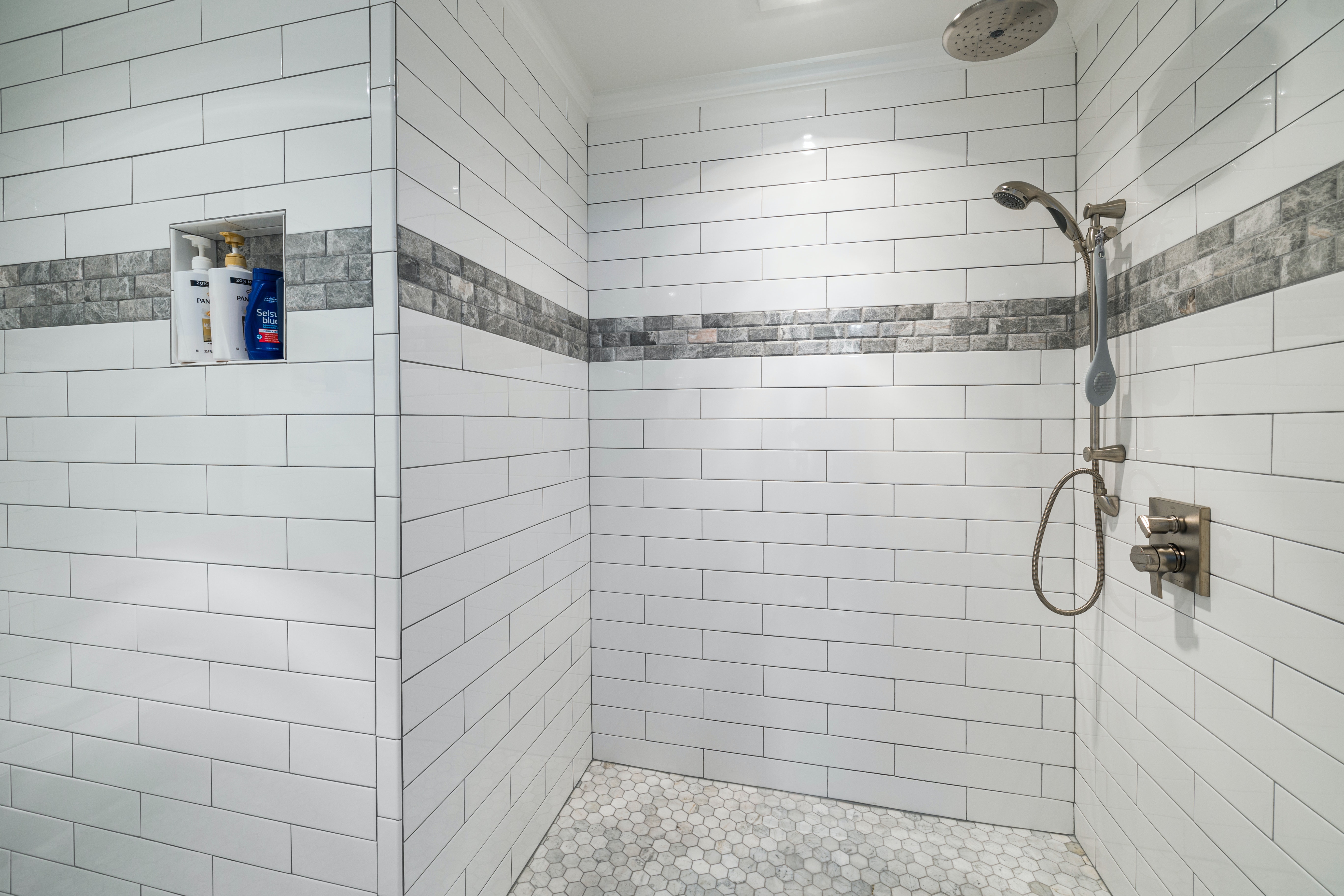 A sleek, walk-in shower enclosure accented by white horizontal metro tiles, finished with stone-effect border tiles.