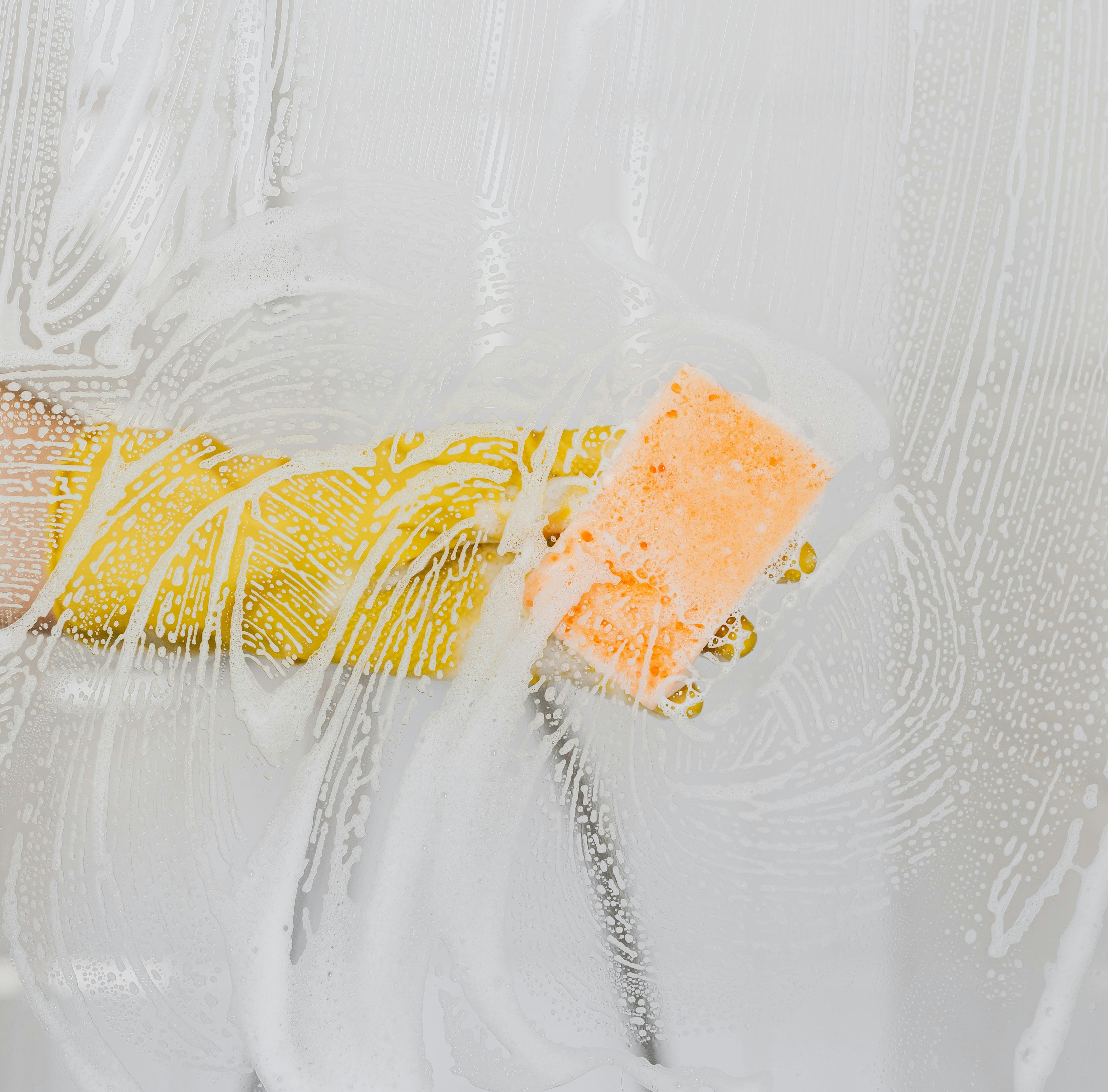 Person scrubbing a glass shower screen with a sponge