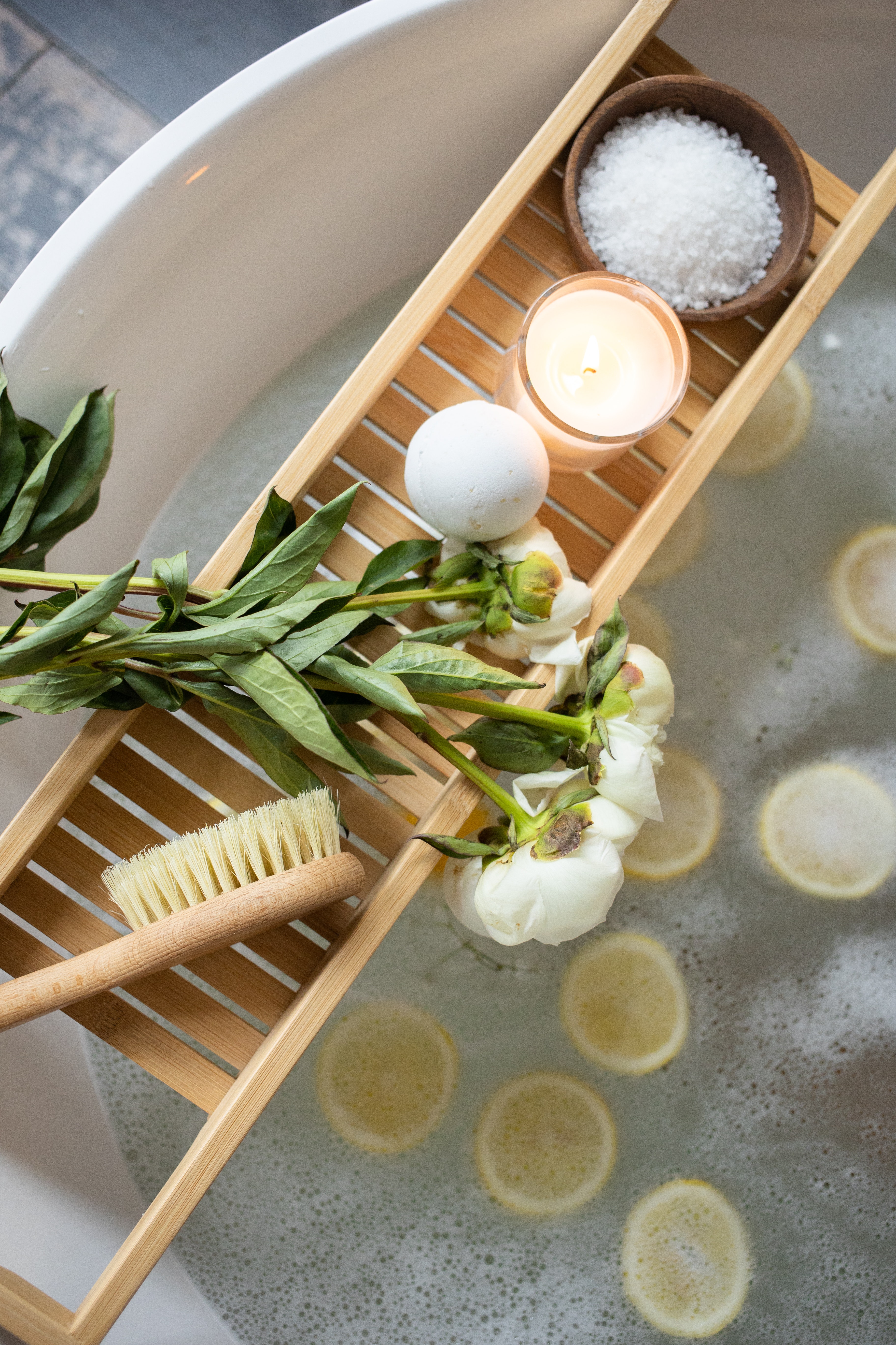 Tray with candles, bath bomb, bath salts and flowers on bathtub